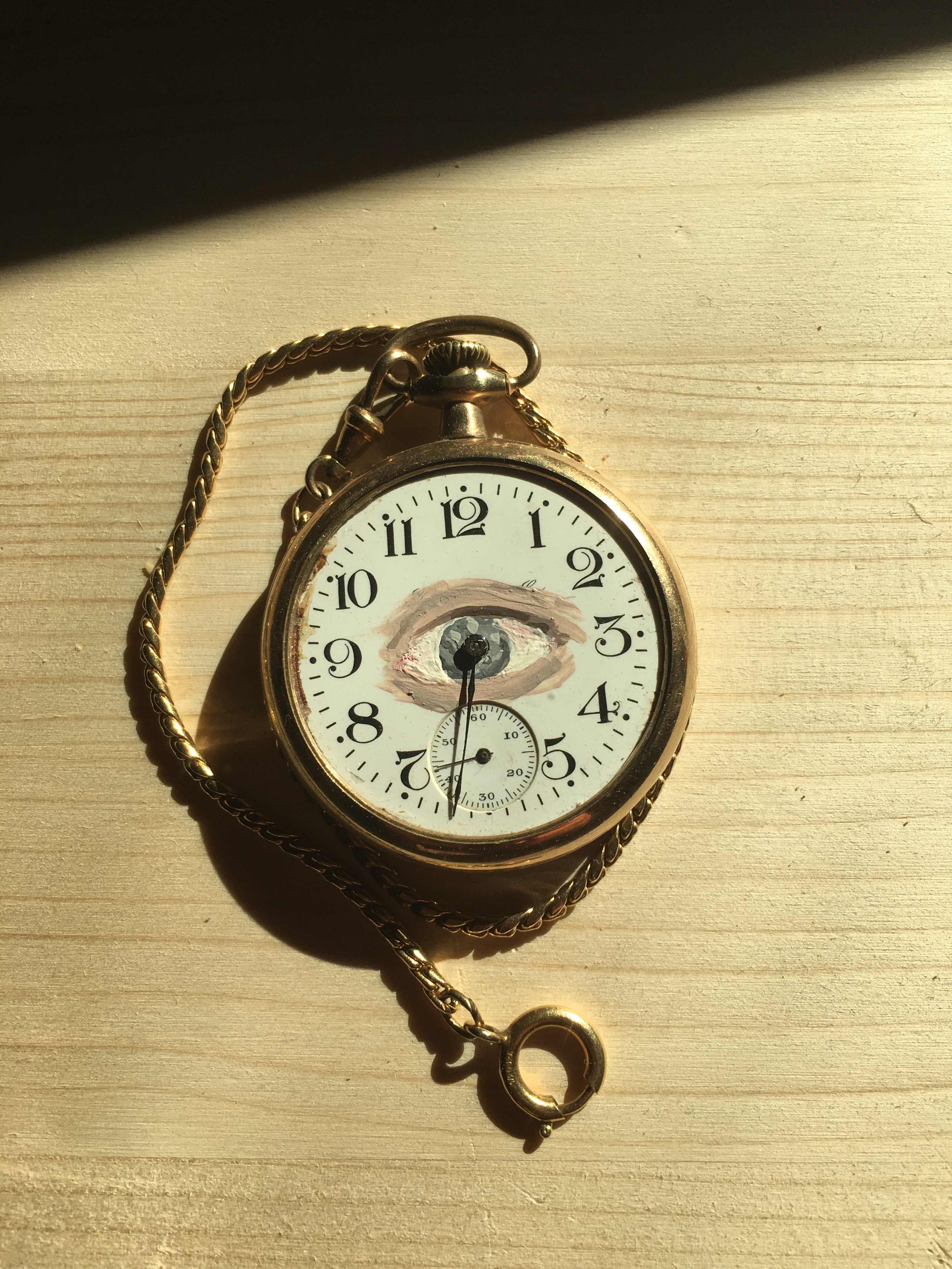 A gold picket watch with an eye painted on the face. The pupil of the eye is centered on the hands of the clock